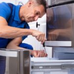 Mature,Male,Serviceman,Repairing,Refrigerator,With,Toolbox,In,Kitchen