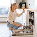 Smiling,Young,White,Woman,Putting,Dishes,In,The,Dishwasher,At